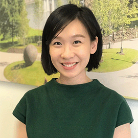 A smiling woman stands in front of a green landscape as she looks directly at the camera.
